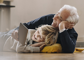 Memory care services. Happy grandfather and grandson lying on floor while watching something on a tablet.